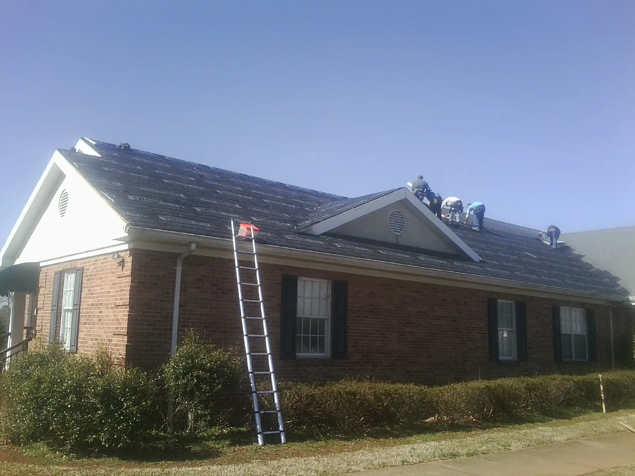 Crew tearing shingles off a brick ranch roof with a ladder set — Metal Roof Repair work by our crew in Nooksack