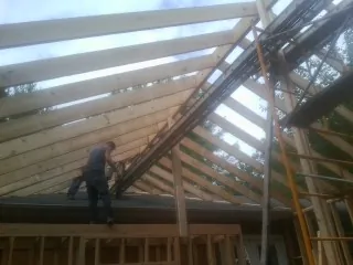 Rafters going up over a new addition with a worker on the wall in Nooksack