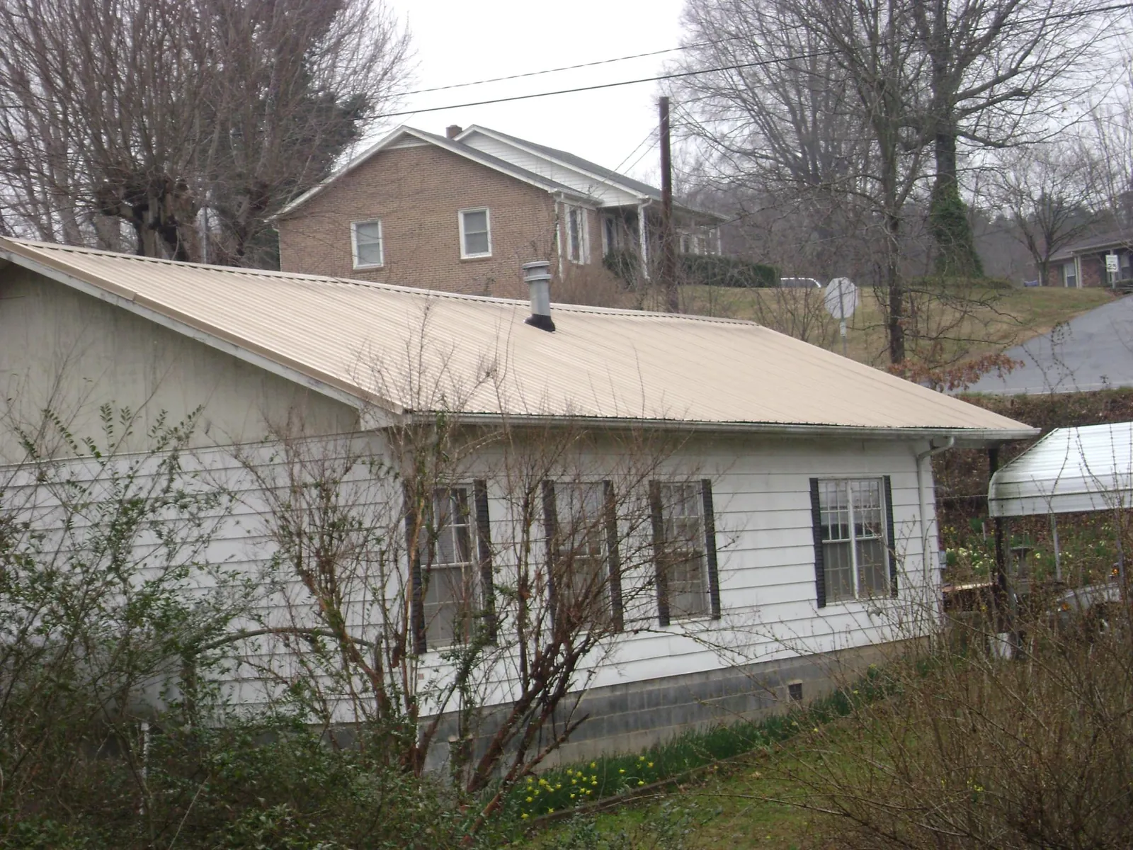 Tan metal roof on a white sided house set into a hillside — Commercial Roofing by Roofing Brothers in Nooksack